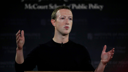 Mark Zuckerberg stands gesturing wearing a black shirt in front of a dark background.