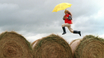 child with yellow umbrella jumping over haystacks