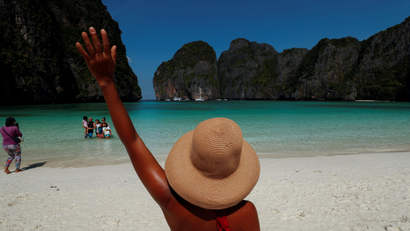 A person in a hat waves towards the beach in Thailand