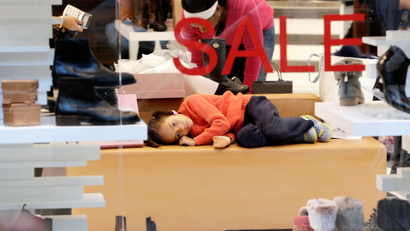 A young girl lies on a couch as the woman she was accompanying checks out shoes while shopping on Black Friday at the Garden State Plaza mall Friday, Nov. 28, 2014, in Paramus, N.J. (AP Photo/Julio Cortez)
