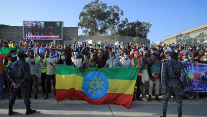 Ethiopian police stand guard during a pro-government rally in Addis Ababa. Hundreds of people stand behind an Ethiopian flag on the street during the daytime.