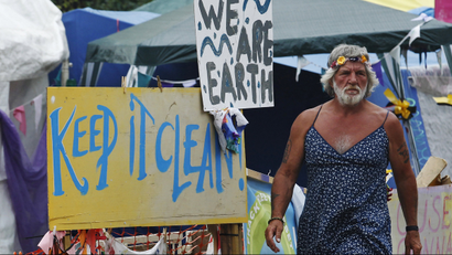 A man wearing a dress walks past signs at the protest camp in front of a drill site run by Cuadrilla Resources, in the village of Balcombe in southern England September 3, 2013. Caudrilla Resources's site in the village of Balcombe in rural West Sussex has become a focal point for protesters who oppose fracking, a technique the company has pioneered in the search for shale gas in Britain.