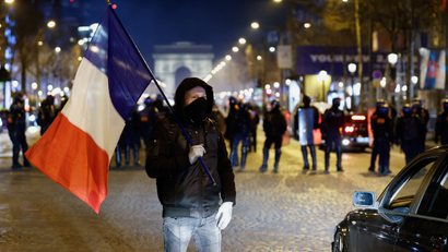 A man stands with a French flag in front of the Arc de Triomphe at an anti-government protest.