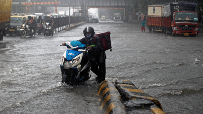 Delivery boy pushes his scooter after it stopped working along a waterlogged road following heavy rainfall in Mumbai