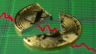 Broken representation of the Bitcoin virtual currency, placed on a monitor that displays stock graph and binary codes, are seen in this illustration picture