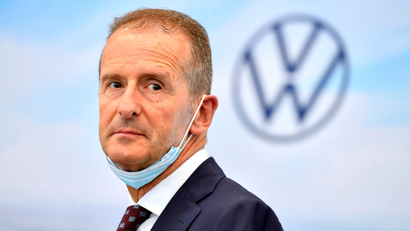 Volkswagen CEO Herbert Diess is pictured in front of the car company's logo with a mask below his mouth.