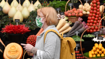 A woman in the UK with a mask on walks past a vegetable stall.