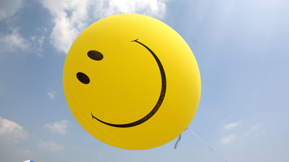 A smiley face balloon floats across a blue sky