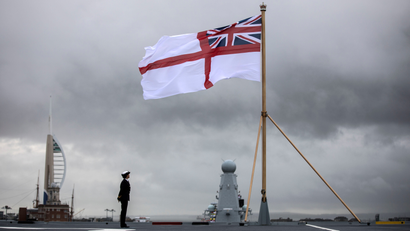 An officer stands on the deck as the White Ensign flies from the stern of the HMS Queen Elizabeth