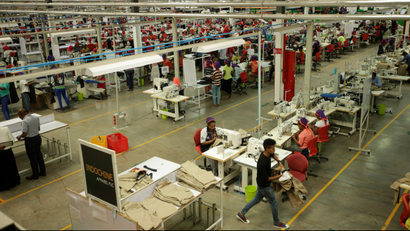 People in a big room work on sewing machines.