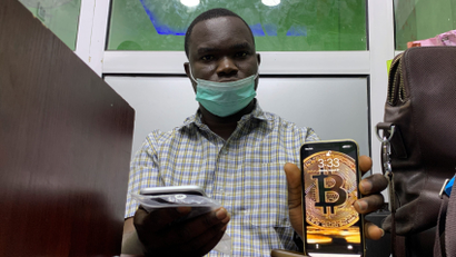 An image of a man posing with a phone that shows a bitcoin-inspired wallpaper