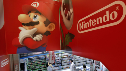 Shoppers walk under the logo of Nintendo and Super Mario characters at an electronics store in Tokyo Wednesday, May 7, 2014. Nintendo Co. sank to a loss for the fiscal year ended March as sales of its Wii U game machine continued to lag, but the Japanese manufacturer of Pokemon and Super Mario games promised Wednesday to return to profit this year. (AP Photo/Shizuo Kambayashi)