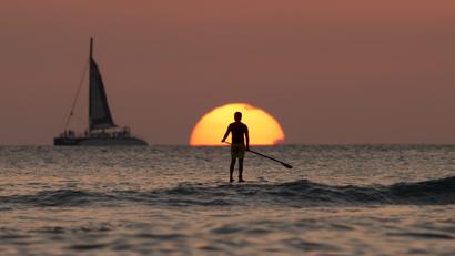 Photo of a person stand-up paddle boarding. They are silhouetted by the setting sun.