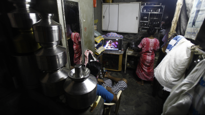 An Indian woman attends to her chores as a man watches on television the Super Eights match between India and Pakistan at the World Twenty20 cricket at a slum in Mumbai, India, Sunday, Sept. 30, 2012. (AP Photo/Rafiq Maqbool