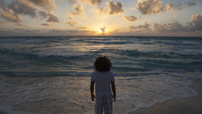 A man faces the sun rising over ocean waves.
