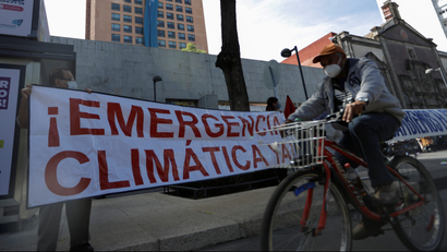 A bicyclist passes as demonstrators hold a sign reading "Climate emergency now" during a protest in Mexico City, 2021. REUTERS/Luis Cortes