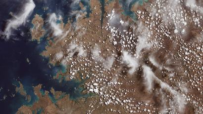 White specs and clouds dot over remote coastal islands and inlets of the Kimberly region of Western Australia in the color, surrounded by the Indian Ocean.