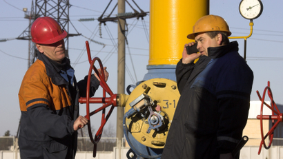 A worker turns a valve as another worker talks on a phone at a gas compressor station at the Yamal-Europe pipeline near Nesvizh.