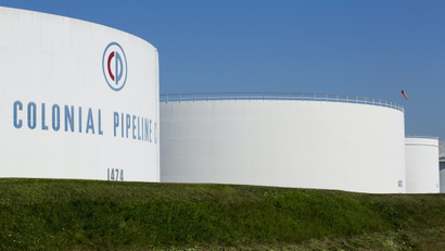 Holding tanks bearing the Colonial Pipeline logo loom over a grassy field.