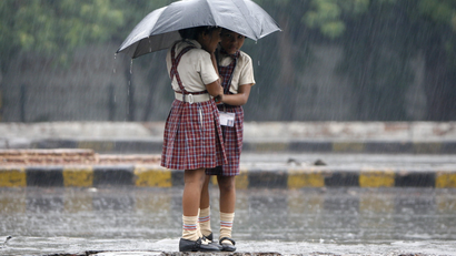 Schoolgirls stand on a road divider as they huddle under an umbrella.