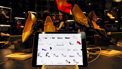 A tablet displays the Shoes of Prey website as Carmen Dang, a design consultant, stands next to designs being showcased in a large department store in central Sydney, Australia, October 1, 2015. Jodie Fox, a co-founder of Australian online retailer Shoes of Prey, which allows customers to design their own footwear, hopes to one day allow customers to print out pairs at home as technology improves and consumer demand grows for personalised products. Founded in 2009, Shoes of Prey allows women to create unique designs on its website, choosing from 300,000 trillion possible permutations of materials, colours, styles and sizes. It promises to deliver in four weeks but often manages two.