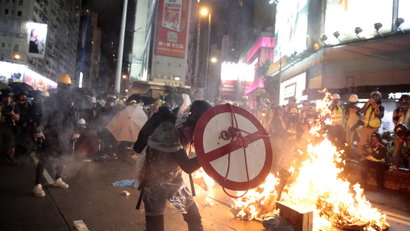 A protester with a shield run past fires in Causeway Bay