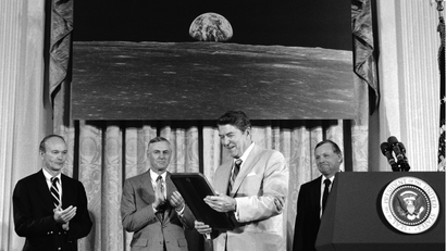 Pres. Ronald Reagan, center, admires a plaque he was presented by Apollo 11 astronauts during a ceremony at the White House on the 15th anniversary of their mission to the moon at the White House during a ceremony to proclaim Space Exploration Day, Friday, July 21, 1984, Washington, D.C. Behind the President, from left are, Michael Collins, NASA Administrator James Beggs; Reagan; and Neil Armstrong.