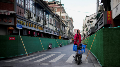 A delivery worker standing on a scooter looks over barriers in a closed residential area during the Shanghai lockdown.