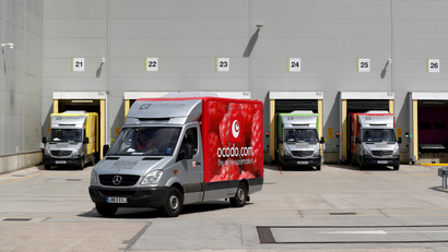 Ocado delivery trucks leave a facility.