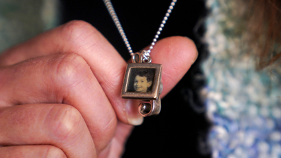 A close-up of a hand holding a locket with a picture of a Sandy Hook shooting victim.
