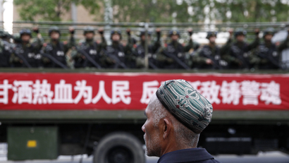 A Uighur man looks on as a truck carrying paramilitary policemen travel along a street during an anti-terrorism oath-taking rally in Urumqi, Xinjiang Uighur Autonomous Region May 23, 2014. China launched a one-year campaign against terrorist violence in Xinjiang Uighur Autonomous Region on Friday, after 39 people were killed and 94 injured in a terrorist attack on Thursday, Xinhua News Agency reported. The Chinese characters on the banner read, "Willingness to spill blood for the people. Countering terrorism and fighting the enemies is part of the police spirit." Picture taken May 23, 2014. REUTERS/Stringer (CHINA - Tags: CIVIL UNREST MILITARY POLITICS) CHINA OUT. NO COMMERCIAL OR EDITORIAL SALES IN CHINA - GM1EA5O19KT02