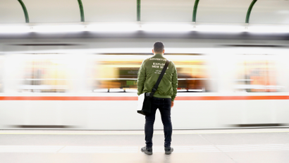 A man waits on platform as subway rushes by in Vienna.