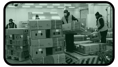 A picture of workers in a warehouse loading cartons of goods on a machine