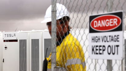 A worker in a hard hat stands in front of a Tesla battery installation.