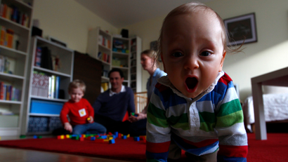 a baby crawls toward the camera with parents in the background