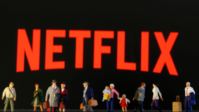 Small toy figures are seen in front of diplayed Netflix logo