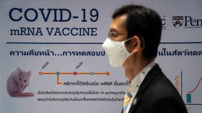 A man wearing a face mask stands next to a board showing the progress of developing an mRNA type vaccine candidate for the coronavirus disease