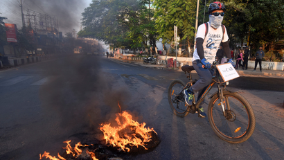 A cyclist passes burning tyres set ablaze by protesters during the strike called by AACSU to protest against the bill in Guwahati