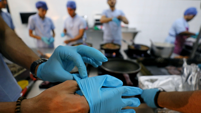 A doctor puts on blue surgical gloves. Their surgical team is in the background also getting ready wearing scrubs and masks.
