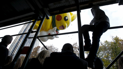 People watch through scaffolding as the "Pikachu" balloon floats down Central Park South during the 89th Macy's Thanksgiving Day Parade in the Manhattan borough of New York