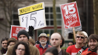 protesters wearing red shirts hold signs advocating for a $15 minimum wage