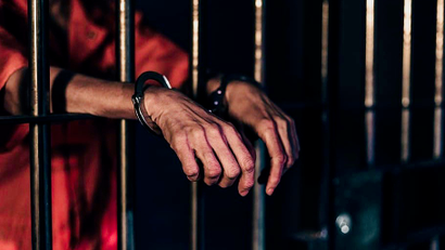 Man in handcuffs behind prison bars.