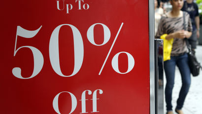In this July 19, 2012 photo, a shopper in New York passes a sign for discounted clothing.