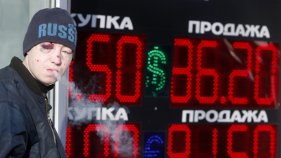 A man smokes near a board showing currency exchange rates of the U.S. dollar and euro against the rouble in Moscow