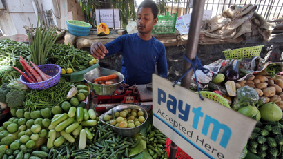 A vendor weighs vegetable next to an advertisement of Paytm, a digital payments firm, hanging amidst his vegetables at a roadside market in Mumbai