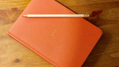 An image of a pink journal that says "Goals" with a white sharpened pencil on top against a wooden background.