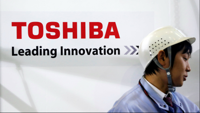 An employee stands next to a logo of Toshiba Corp in Yokohama, south of Tokyo November 21, 2012.