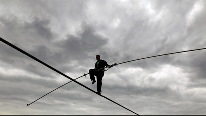 A man walks across a tightrope against a cloudy sky.