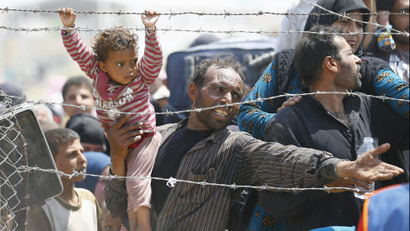 A Syrian refugee reacts as he waits behind border fences to cross into Turkey