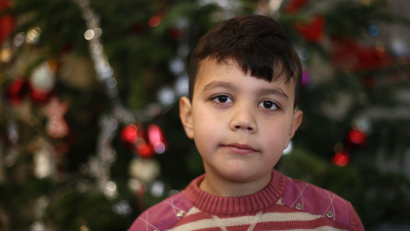 Seven-year old Karam of Syria poses in front of a Christmas tree at a refugee shelter in an evangelic church in Oberhausen, Germany, December 22, 2015